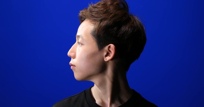 Portrait of Asian young man with dark and bright side of face turning his head on blue screen background