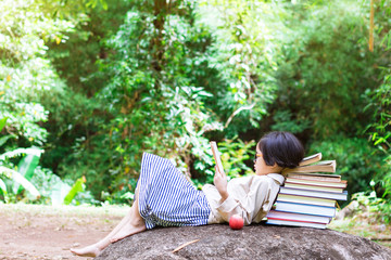 Fototapeta premium Asian little girl with glasses lying on stone reading a books