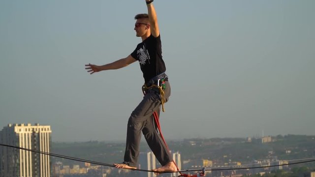 A man in sunglasses is walking on a tight rope against the background of the city