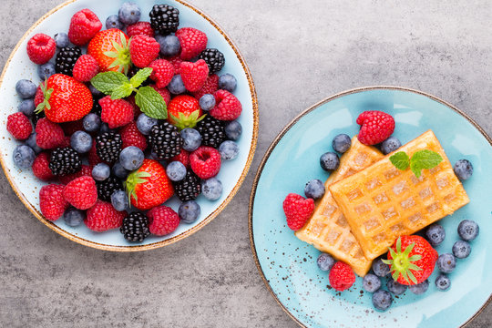 Homemade waffles with berries salad on blue dishes. Vintage wooden background.