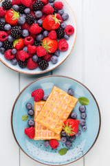 Homemade waffles with berries salad on blue dishes. Vintage wooden background.
