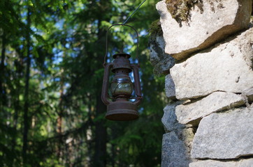 An old lantern hanging on an old stone house in a forest