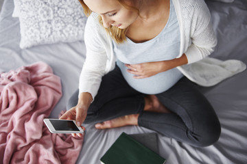 Pregnant woman using mobile phone at bedroom