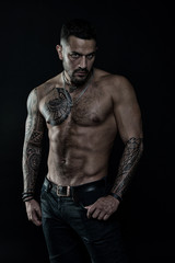 Fototapeta na wymiar Tattoo model with six pack and ab. Bearded man with tattooed body. Man with sexy bare torso in jeans. Athlete or sportsman with muscular chest and belly. Sport or fitness and bodycare, vintage filter