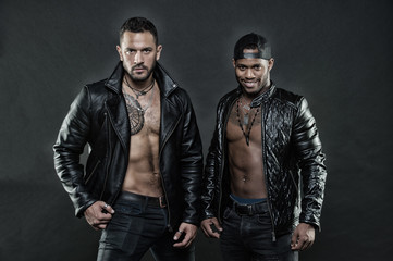 Machos with muscular torsos look attractive in leather jackets, dark background. Men on confident...