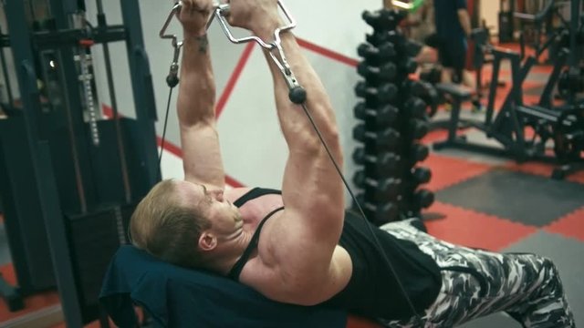 Bodybuilder in gym machine doing incline cable fly for pecs, slow motion, shallow depth of field
