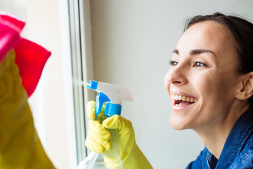 Beautiful Young Woman is Using a Duster and a Spray and Smiling While Cleaning Windows in the House