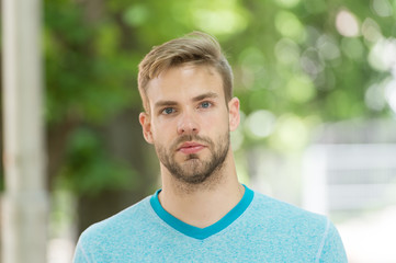 Man with bristle on calm face, nature background, defocused. Man with beard or unshaven guy looks...