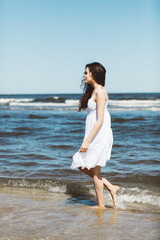 Fototapeta na wymiar A girl in white dress walking alongside the ocean.