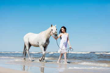 Girl walking on the beach with white horse.