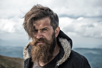Man with brutal bearded appearance, brutal unshaven man looks untidy. Man with long beard and mustache wears jacket. Hipster on strict face with beard looks brutally while hiking. Hermit concept - obrazy, fototapety, plakaty