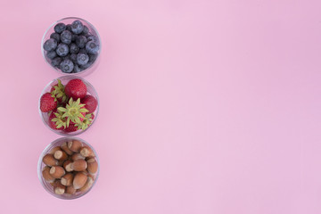Obraz na płótnie Canvas Srawberry, blueberry and hazelnuts in glass cups on pink background