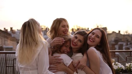 Attractive caucasian girls are hugging standing outside on a terrace or balcony. Six beautiful young women in white shirts and with red lipstick. Hen party. Evening dusk. Love and friendship - Powered by Adobe