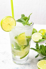 Mojito cocktail with fresh limes and mint leaves in a glass on a light grey stone background