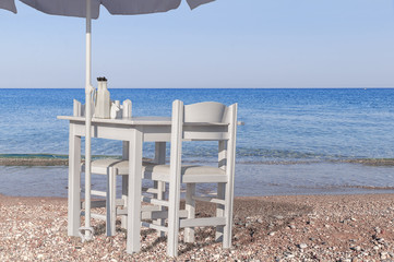Fototapeta premium Two white chair and umbrella with wooden table on pebble beach