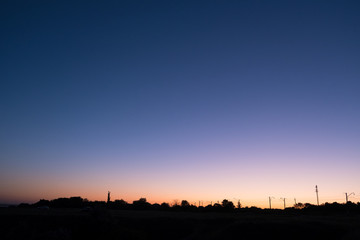 dark blue evening sky with pink sunset strip with black outlines silhouettes of houses background