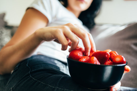 Woman Sitting On Couch And Eating Strawberries Out Of Bowl. Healthy Eating, Vegetarian Food, Fruit.