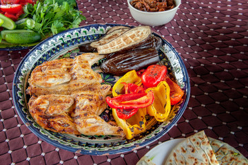 Grilled tobacco chicken with sauce on a stone plate with Bulgarian fried red pepper eggplant zucchini and garlic. Delicious dinner.