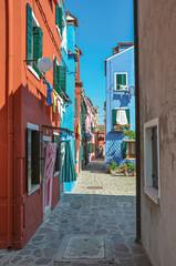 Fototapeta na wymiar Overview of colorful terraced houses and clothes hanging in an alley on sunny day in Burano, a gracious little town full of canals, near Venice. Located in the Veneto region, northern Italy