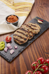 Grilled Veal minced meat with spices on black stone and wooden background 
