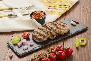 Grilled Veal minced meat with spices on black stone and wooden background 