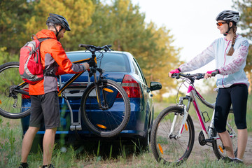 Young Couple Unmounting Mountain Bikes from Bike Rack on the Car. Adventure and Family Travel Concept.