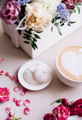 Delicious fresh morning cappuccino coffee with heart latte art on it, little white marshmallows and a basket of blossoming  flowers on the pastel pink background, top view, flat lay