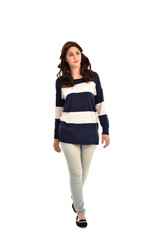 full length portrait of girl wearing striped blue and white jumper and jeans. standing pose on white studio background