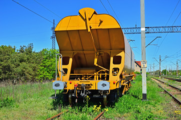 Żółty wagon towarowy stojący na bocznicy kolejowej.