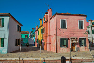 Fototapeta na wymiar Overview of colorful buildings and clothes hanging in a blue sunny day, in front of a canal at Burano, a gracious little town full of canals, near Venice. Located in the Veneto region, northern Italy