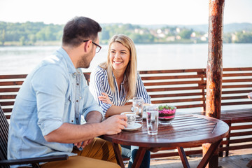 Young couple enjoying time in a riverside cafe. Drinking coffee and talking. Danube in background.