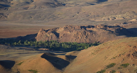 Colorful rocky landscape view of a small forested valley between red mountains