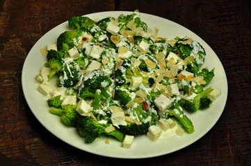 Broccoli with feta and almond flakes on a white plate on a wooden background