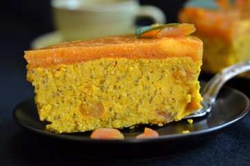 A piece of pumpkin pie awith jelly on top on a black plate