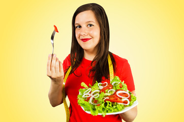Young girl holds plate with salad and eats him, isolated on yellow background.