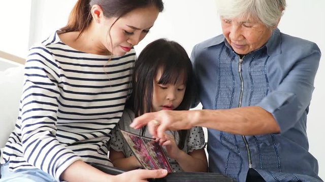 Asian grandmother with her daughter and granddaughter looks an family photos album . 