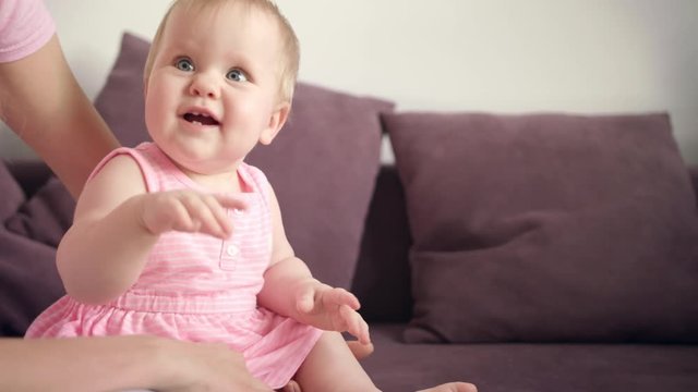 Cute baby child smiling in mother embrace. Close up of sitting kid playing with toy. Beautiful infant sitting on sofa and playing with parents. Sweet childhood. Adorable child laughing at home