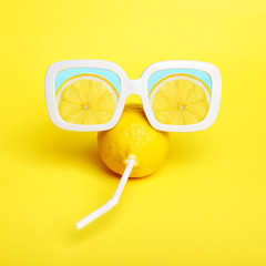 Minimal lemon in sunglasses with straw on yellow.
