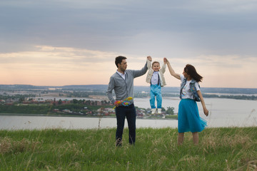 Parents hold their son's hands and raise, the baby jumps, cloudy