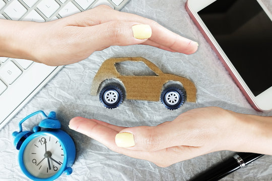 Car insurance concept, woman hands with protective gesture and cardboard car on white background with office objects around
