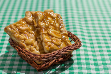 Candy with peanut: Pe de Moleque in Brazil and Chikki in India. Sweet food of Festa Junina, a typical brazilian party. Snack on wicker basket and green background.