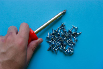The hand holds a red screwdriver. A bunch of nails on a blue background