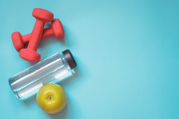 Sport and fitness equipment, dumbbells, water and apple. Creative flat lay on punchy blue. Space...