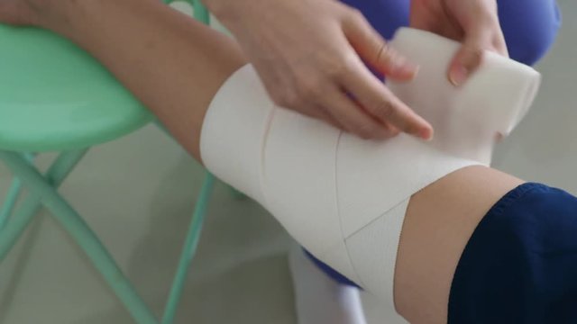 Nurse at the hospital bandaging the knee with a medical bandage for young boy