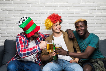 Three happy men sitting on couch and watching sport on TV and cheers beer