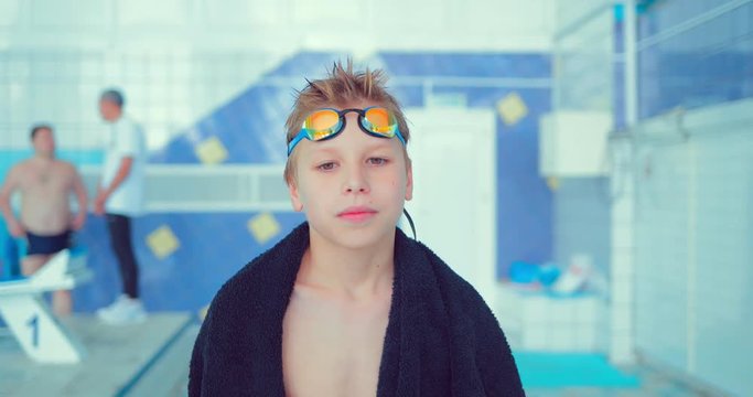 Professional child or swimmer adolescent walks along the pool with a towel on his shoulders to the starting block to begin swimming training