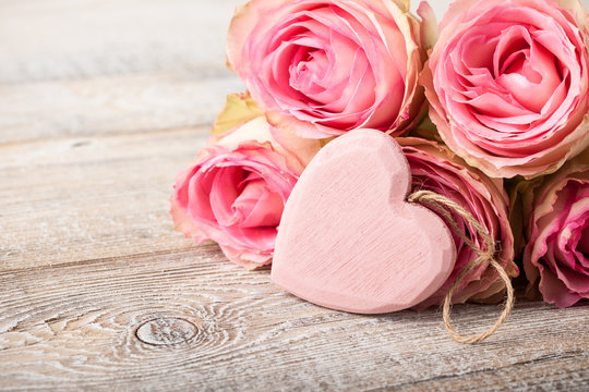Fresh pink roses and heart decoration on wooden boards
