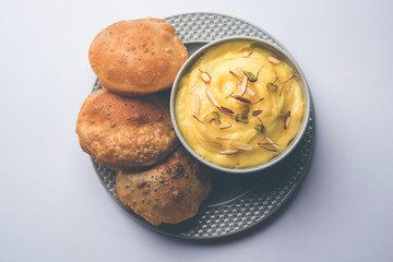 Shrikhand with fried Puri / Poori served in a bowl and plate over moody background. Selective focus