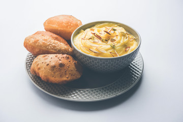 Shrikhand with fried Puri / Poori served in a bowl and plate over moody background. Selective focus