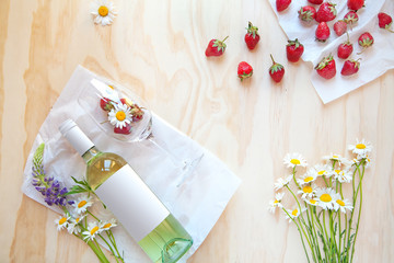 A bottle of white wine on a wooden background with strawberries and flowers